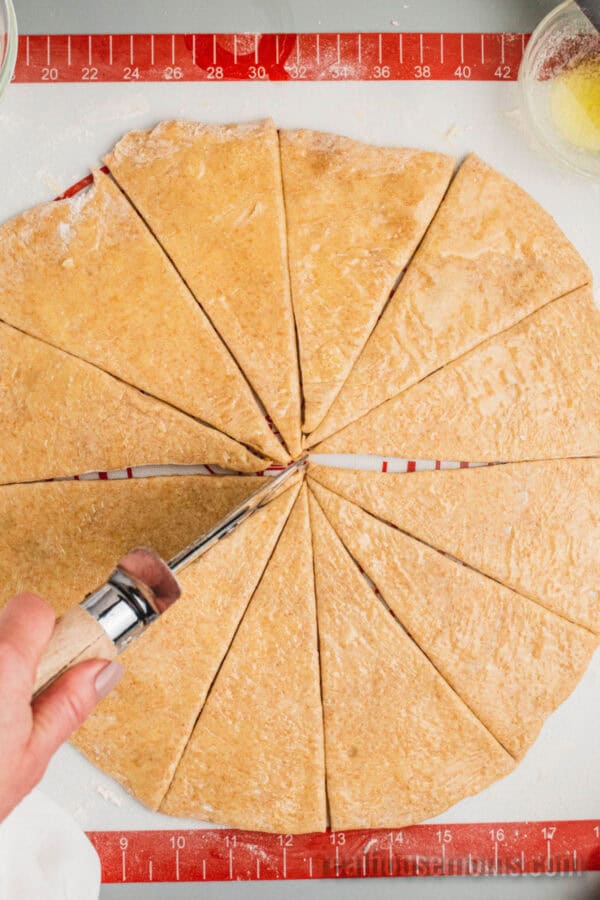 pizza cutter being used to cut a dough disc into wedges