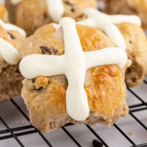 square image of a hot cross bun with orange frosting on a wire rack