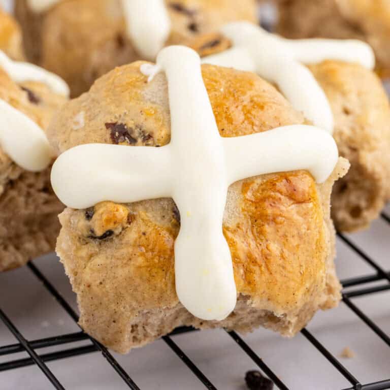 square image of a hot cross bun with orange frosting on a wire rack