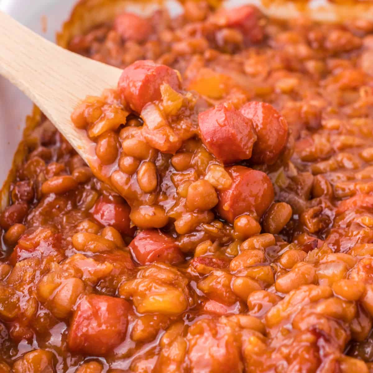 square image of a spoonful of hot dogs and beans over a baking dish