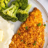 hot honey cornflake chicken on a dinner plate with mashed potatoes and broccoli with the title of the post on top of the image in pink and black lettering