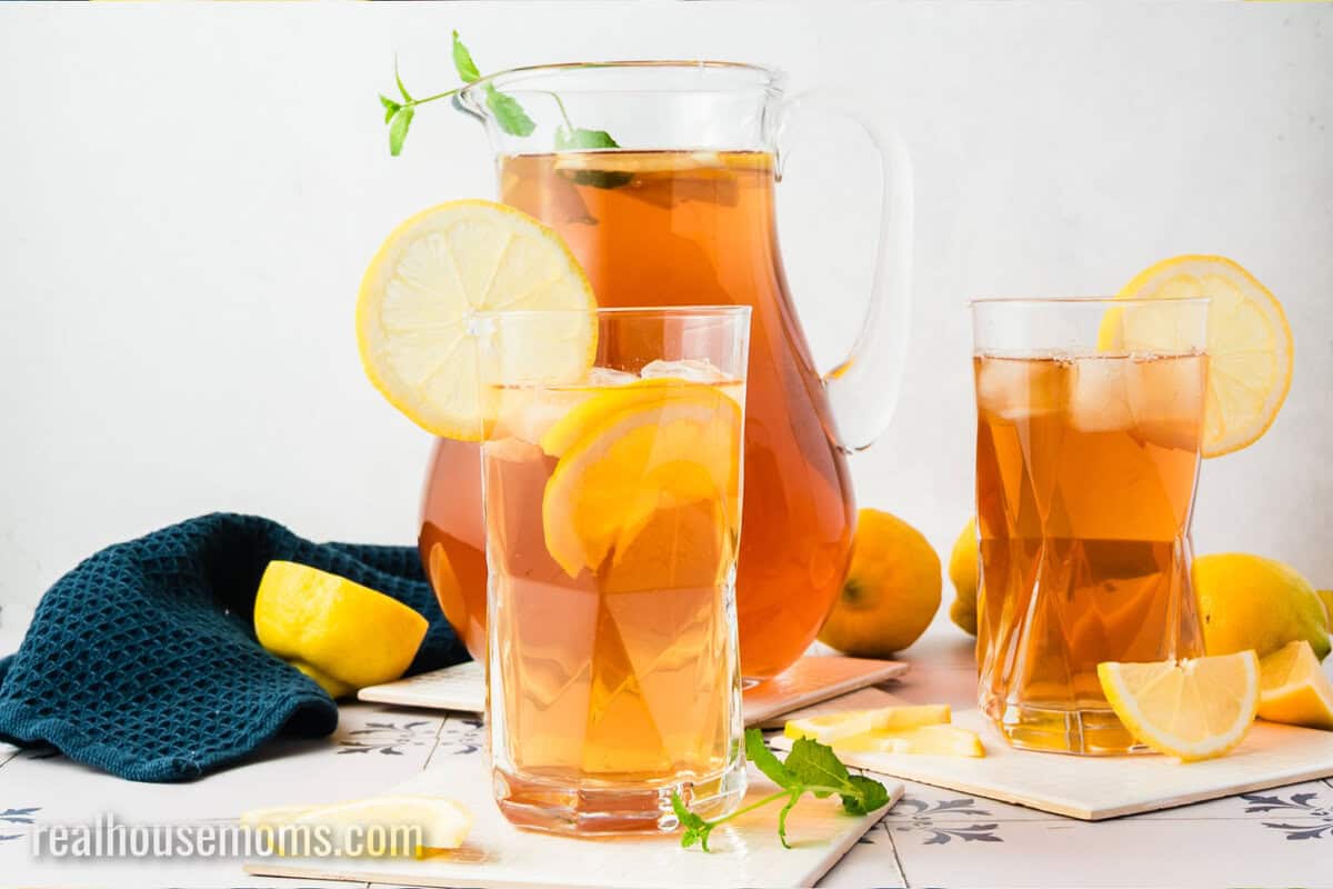 glass of sun tea with ice and lemon slices next to the pitcher