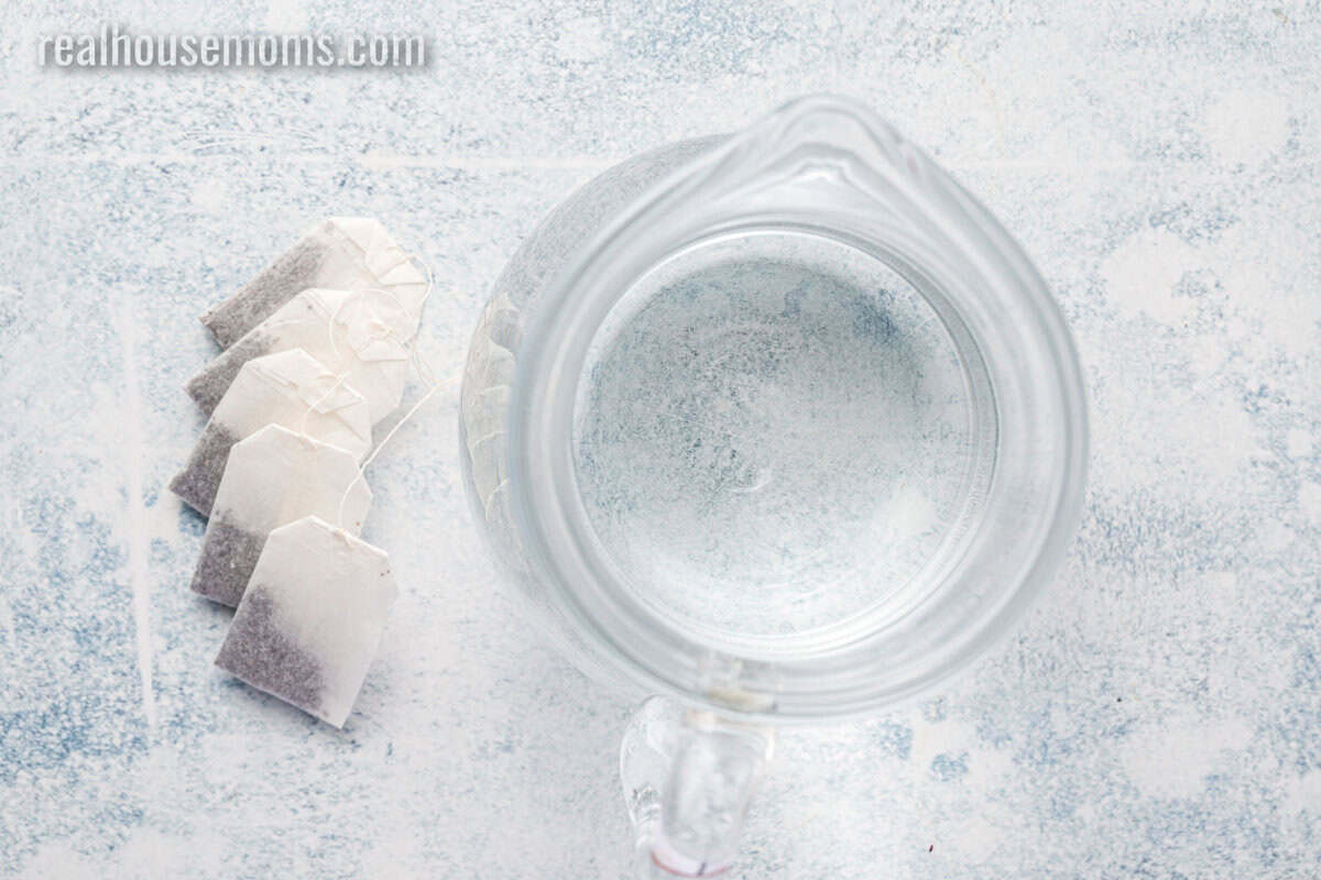 a pitcher of water next to black tea bags on a counter