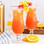 square image of two hurricane cocktails with orange slices and cherries for garnish