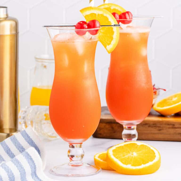 square image of two hurricane cocktails with orange slices and cherries for garnish