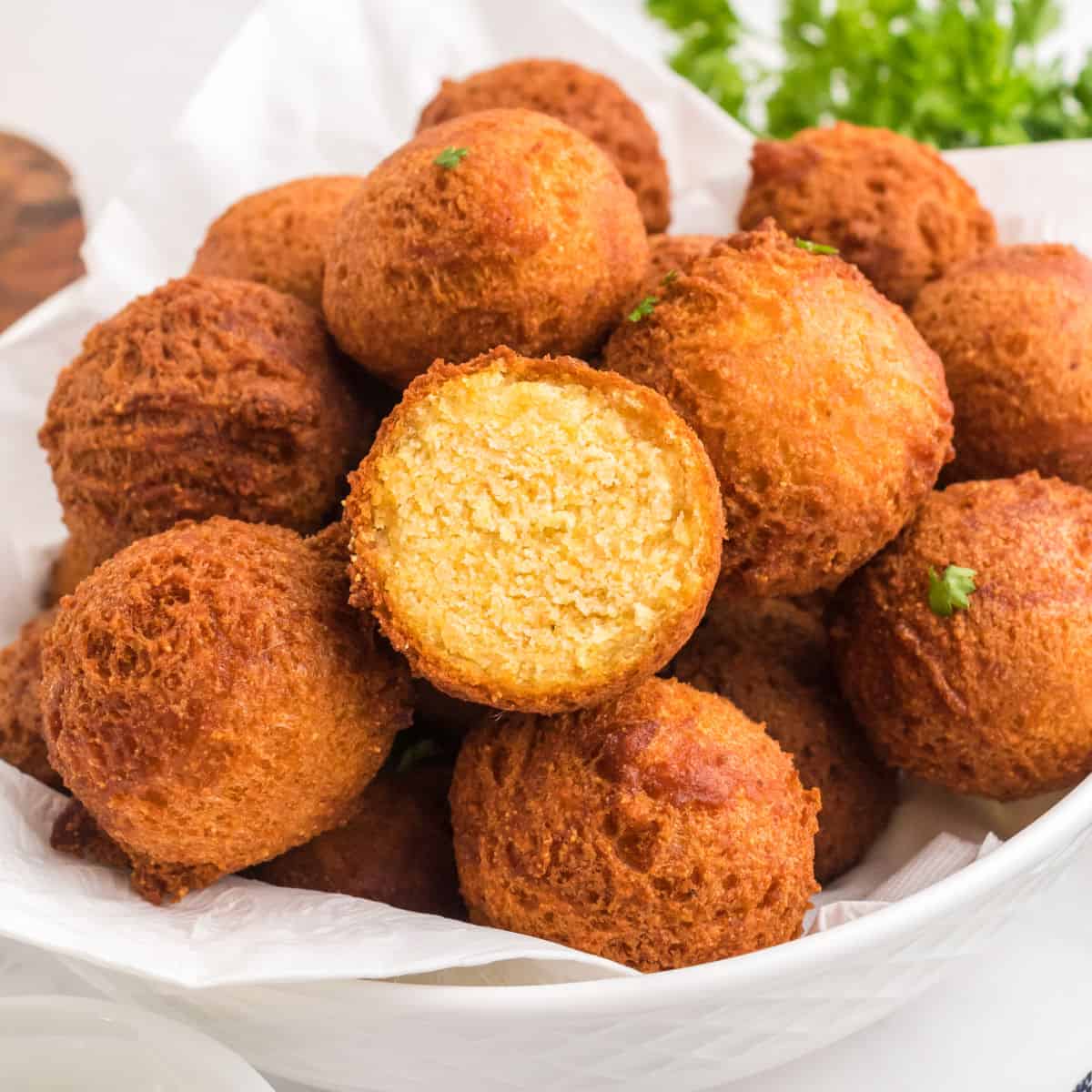 square image of hush puppies piled in a bowl with one cut in half to show the inside