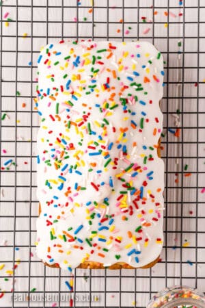 loaf of ice cream bread topped with vanilla glaze and sprinkles on a wire rack