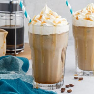 square image of an iced caramel macchiato in front of a french press