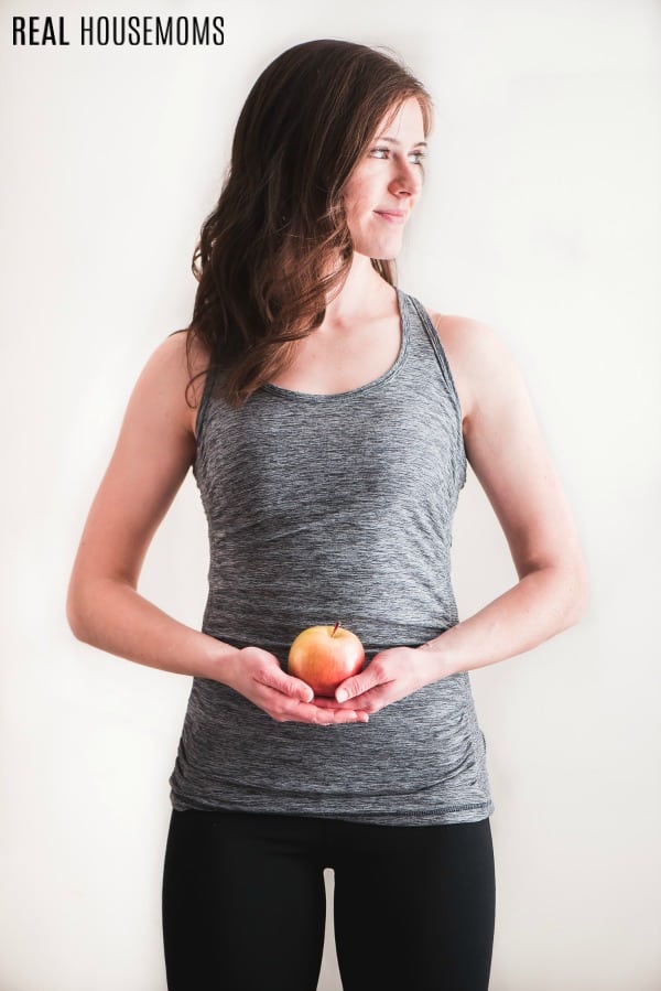woman in workout clothes holding an apple by her stomach