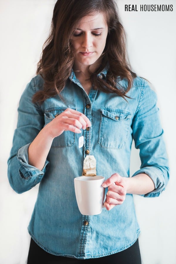 woman removing a tea bag from her cup after steeping