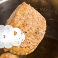 tongs holding a cooked, seasoned pork chop