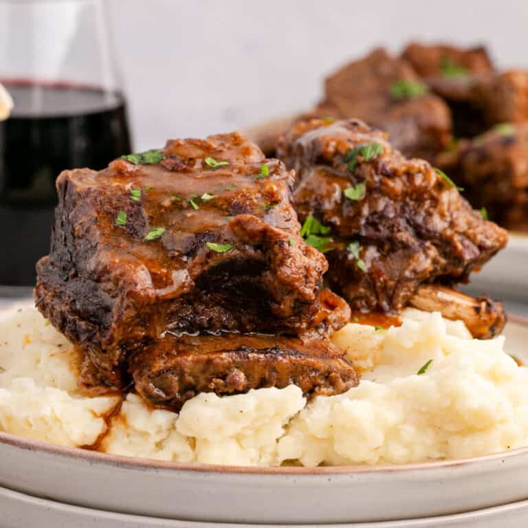 square image of instant pot short ribs with gravy plated over mashed potatoes next to a glass of red wine