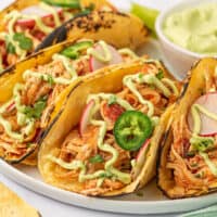 square image of instant pot shredded chicken tacos on a plate next to a bowl or avocado cilantro sauce