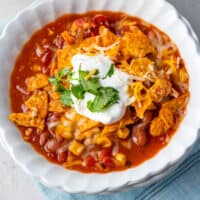 instant pot taco soup in a white bowl topped with doritos, sour cream, cheddar cheese, and cilantro with recipe name at bottom
