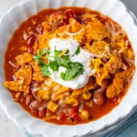 square image of taco soup in a bowl topped with doritos, cheese, sour cream, and cilantro