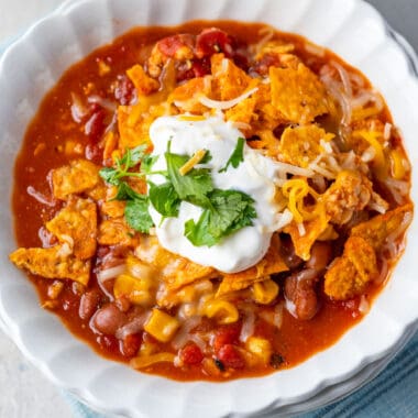 square image of taco soup in a bowl topped with doritos, cheese, sour cream, and cilantro