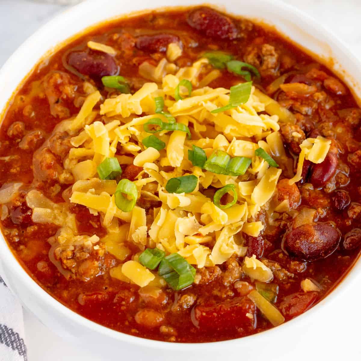 square image of instant pot chili in a bowl with shredded cheddar cheese and sliced green onion