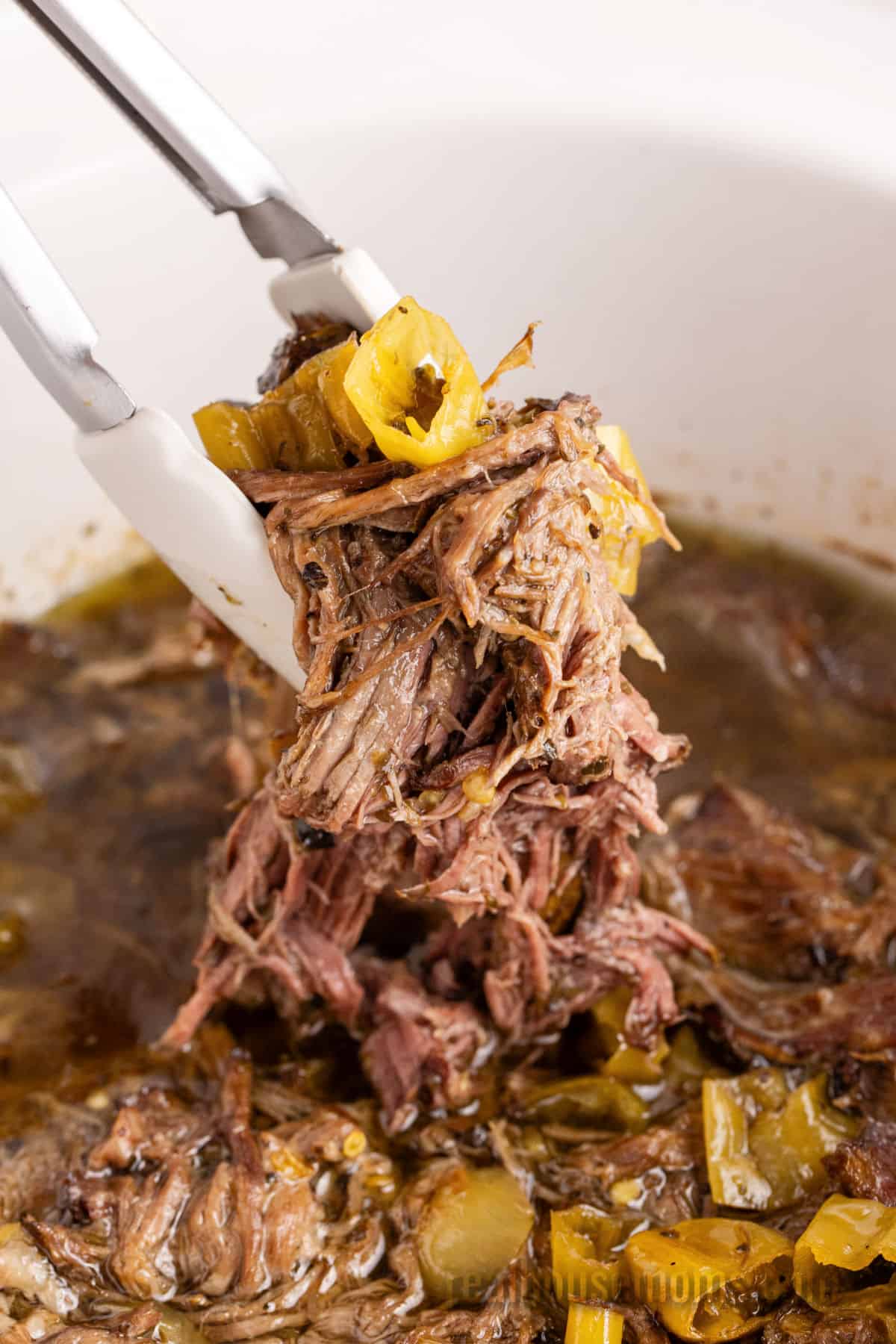 tongs pickup shredded italian beef from the slow cooker