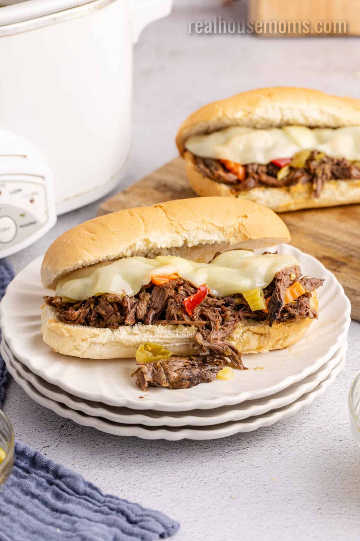 italian beef sandwich with provolone cheese on a white plate next to the slow cooker