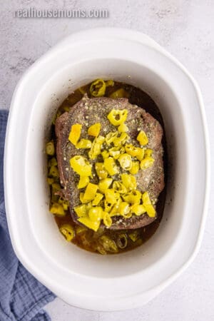 sliced pepperoncini and brine poured over a seasoned chuck roast in a crock pot