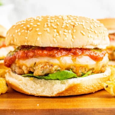 square image of an italian chicken burger on a wooden board with fries