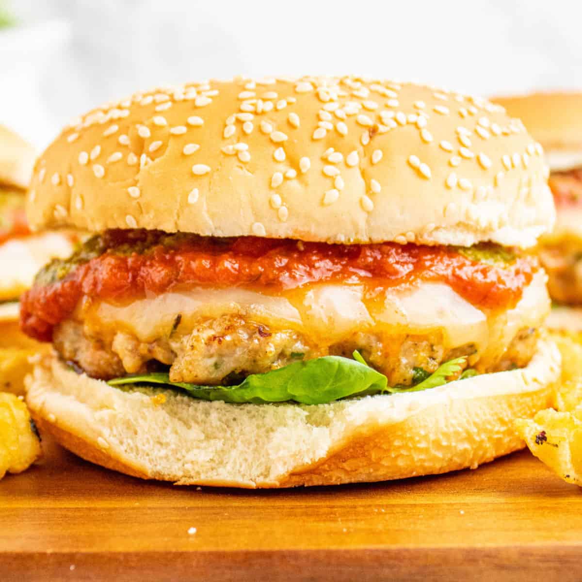 square image of an italian chicken burger on a wooden board with fries