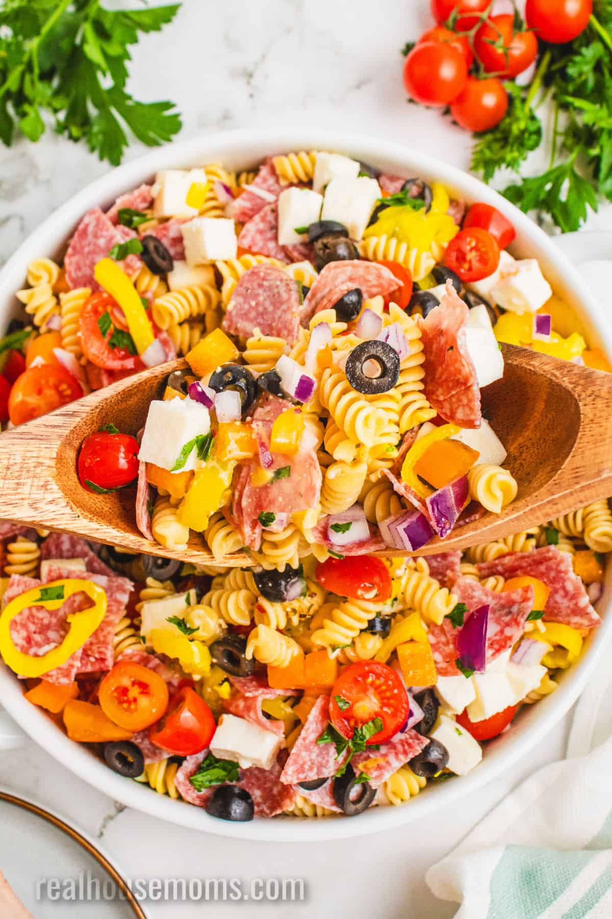 spoons lifting a portion of italian pasta salad from the serving bowl