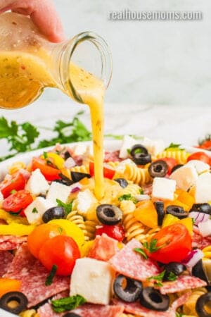 italian dressing being poured over pasta salad