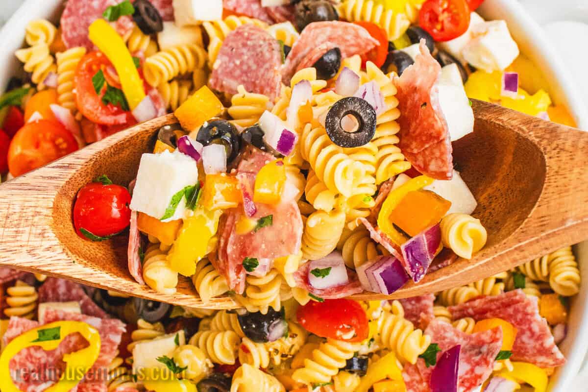 two wooden spoons lifting a portion of italian pasta salad from a serving bowl