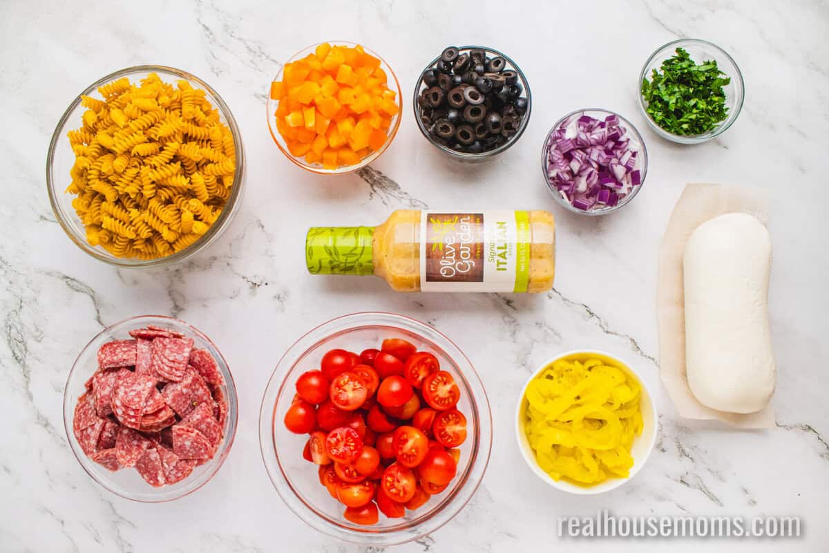 ingredients to make italian pasta salad in bowls on a counter