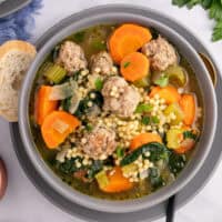 square image of a bowl of italian wedding soup with a spoon and crusty bread