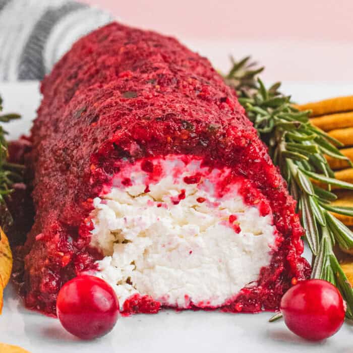 square image of a jalapeno cranberry goat cheese log on a plate with a slice cut off the end