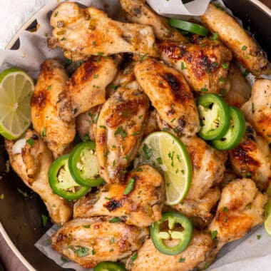 square image of jalapeno lime chicken wings in a serving bowl with lime and jalapeno slices