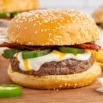 square image of a jalapeno popper burger on a wooden tray next to a jalapeno slice