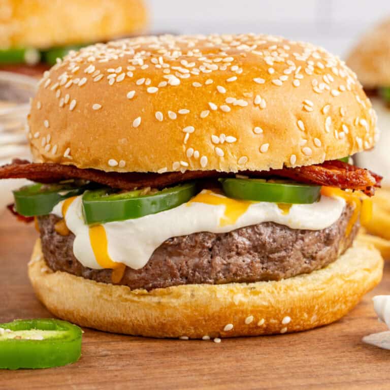 square image of a jalapeno popper burger on a wooden tray next to a jalapeno slice