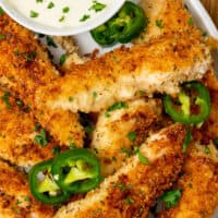 picture of jalapeno ranch chicken tenders on a platter with chopped parsley and jalapeno slices. On top of the picture is the title of the post in pink and black lettering
