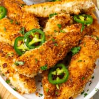 square image of jalapeno ranch chicken tenders on a platter with chopped parsley and jalapeno slices