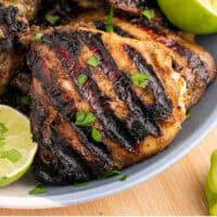 jerk chicken thighs and lime halves on a plate with recipe name at the bottom