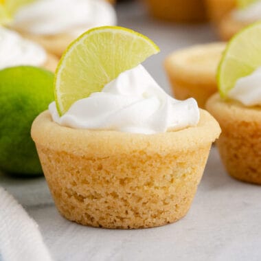 square image of a key lime pie cookie cup topped with whipped cream and half of a lime slice