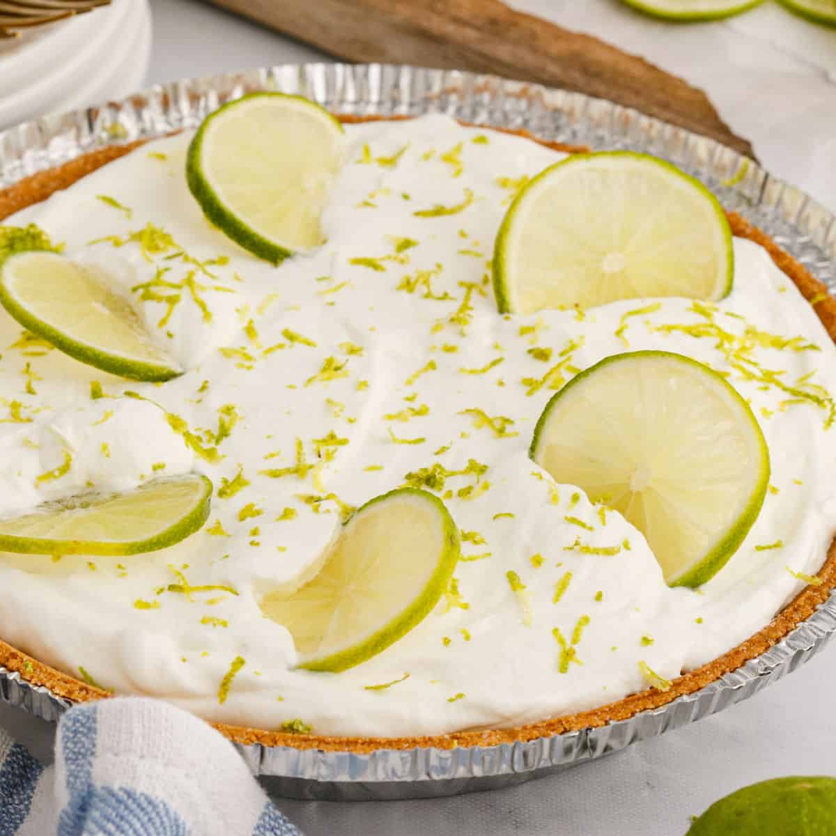 square image of key lime pie in a pie pan with lime zest and slices for garnish