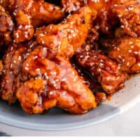 korean fried chicken topped with sesame seeds in a serving bowl with recipe name at the bottom