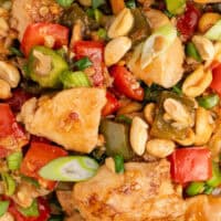 close up image of kung pao chicken served over white rice with chopsticks with the title of the post on top of the image in pink and black lettering