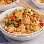 square image of kung pao chicken served over white rice with chopsticks