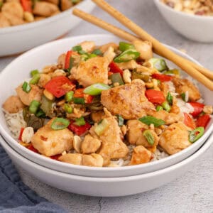 square image of kung pao chicken served over white rice with chopsticks