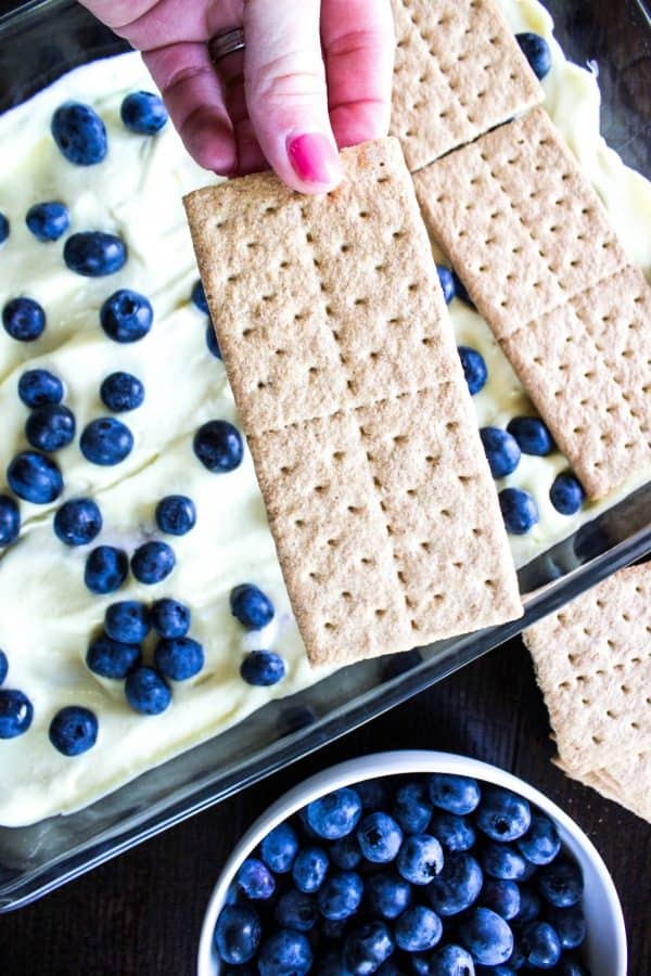 Graham crackers being layered over blueberries and lemon cream in a baking dish