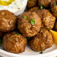 square image of lamb meatballs on a plate topped with chopped parsley