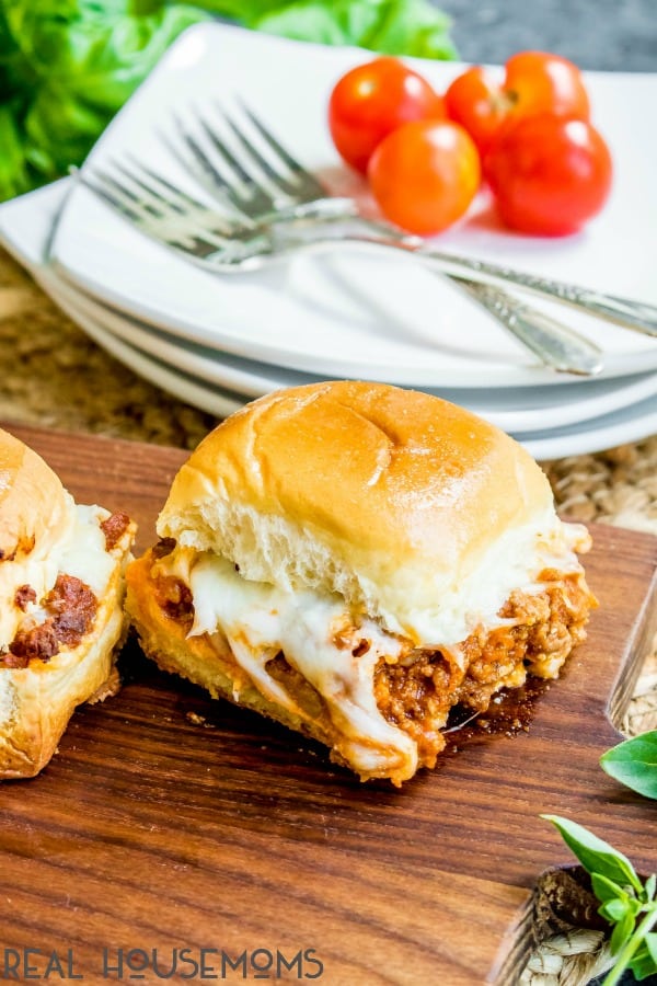 Individual Lasagna Sliders on a cutting board for serving with gooey cheese melting down the side.