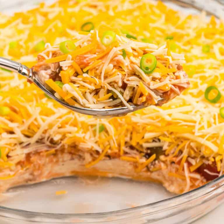square image of a spoonful of layered nacho dip over the pan