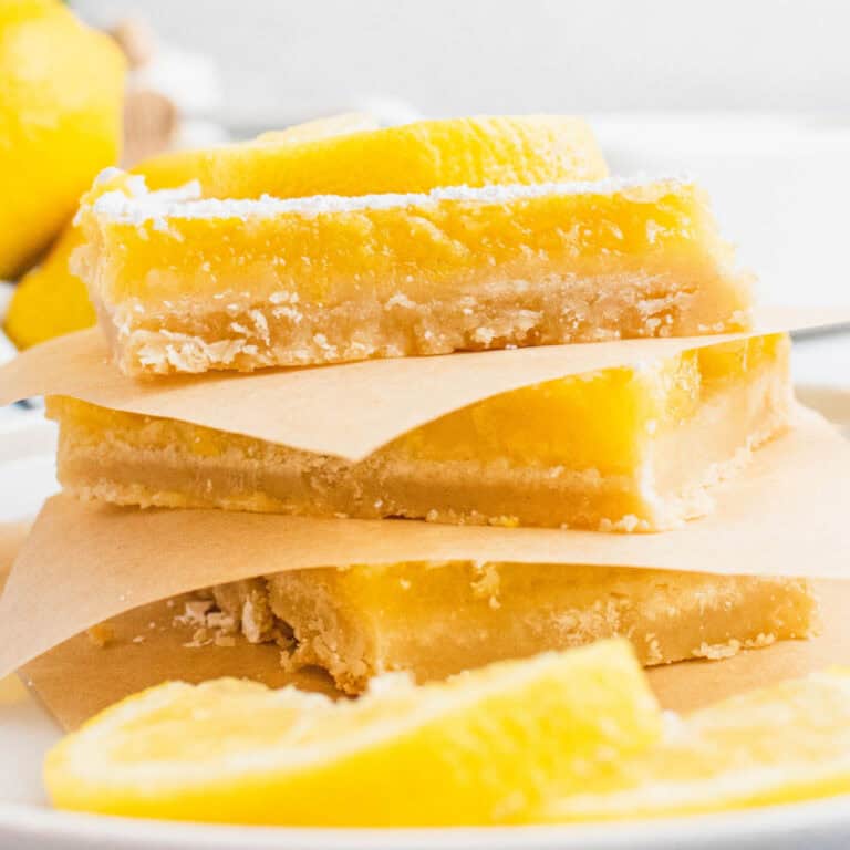 square image of lemon bars stacked up with parchment paper between the bars