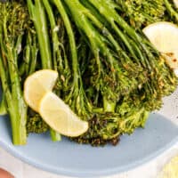 lemon butter broccolini with half lemon slices in a bowl with recipe name at the bottom